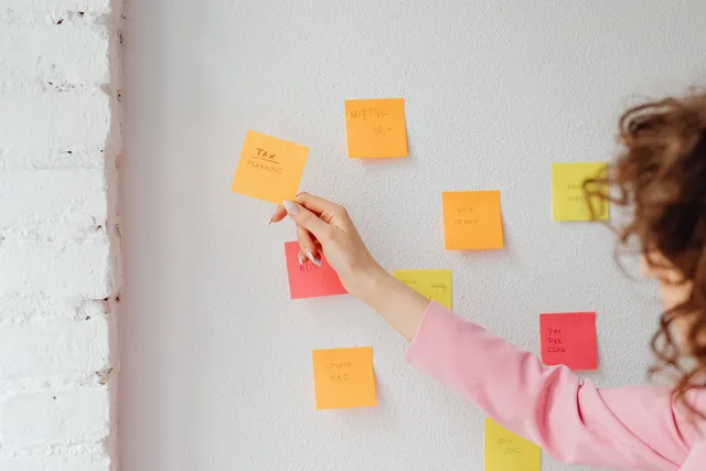 Woman organizing tasks using sticky notes on a wall, promoting productivity and planning. Writing a requirements list from real marketing tasks